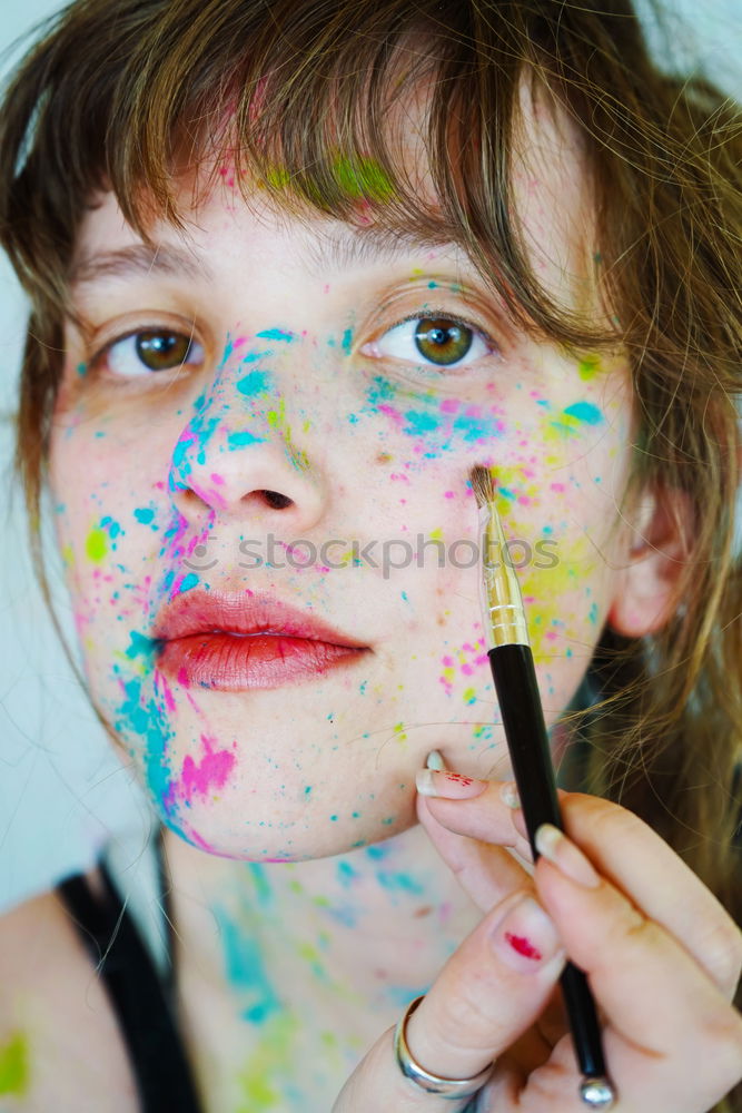 Junge Frau mit Farbe im Gesicht und einem Pinsel.