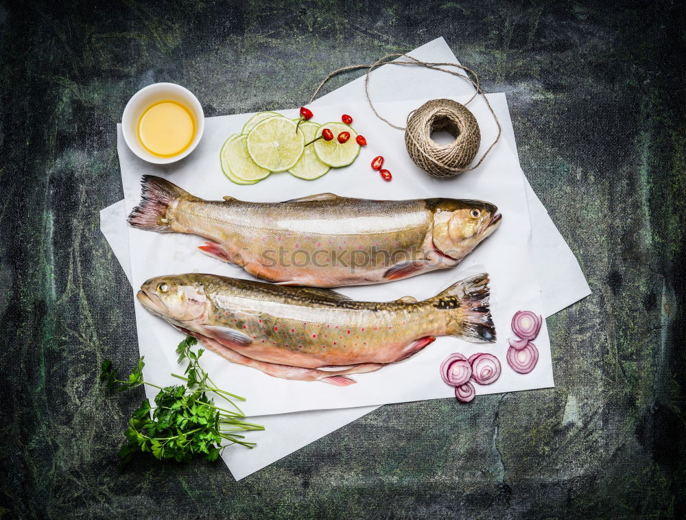 Raw fish on white paper with ingredients for cooking