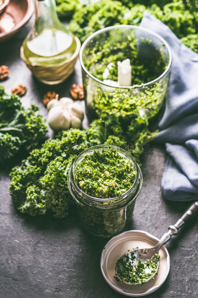 Green kale pesto in glass on dark rustic kitchen table background with ingredients, top view. Kale preparation. Healthy detox vegetables . Clean eating and dieting concept.