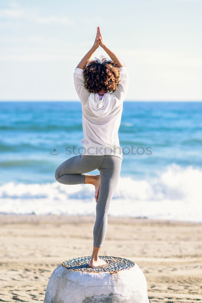 Rear view of young black woman doing yoga in the beach