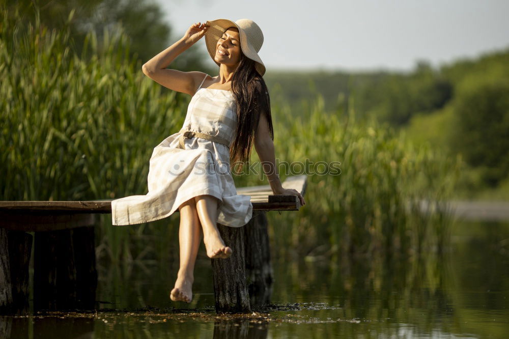 Similar – Young woman in a pink summer dress sitting in a clearing with her feet in the forest lake