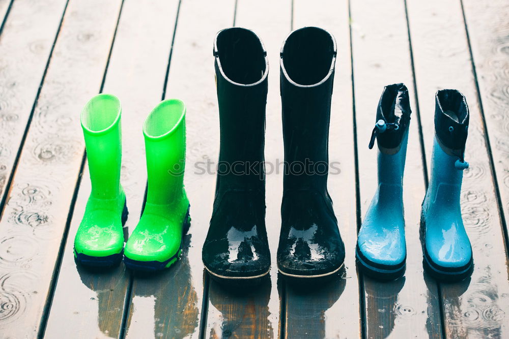 Row of wellies standing on a wooden porch while raining