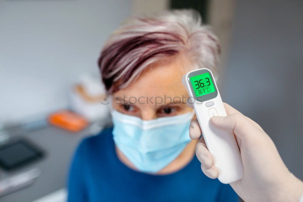 Senior woman without fever whose temperature is taken with an infrared thermometer