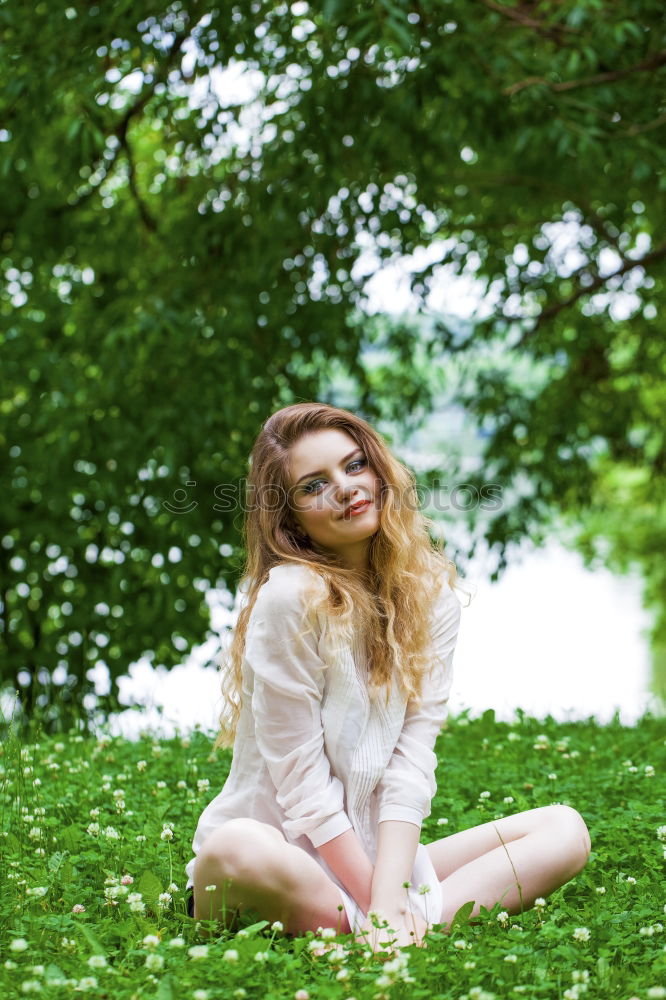 Similar – side portrait of young woman in summer dress sitting barefoot between bushes in nature