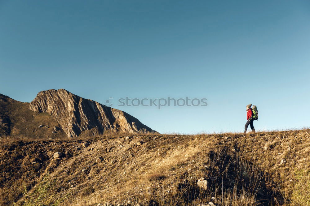 Cloud rolls over the mountains, man with red jacket and backpack stands on a path and looks into a valley