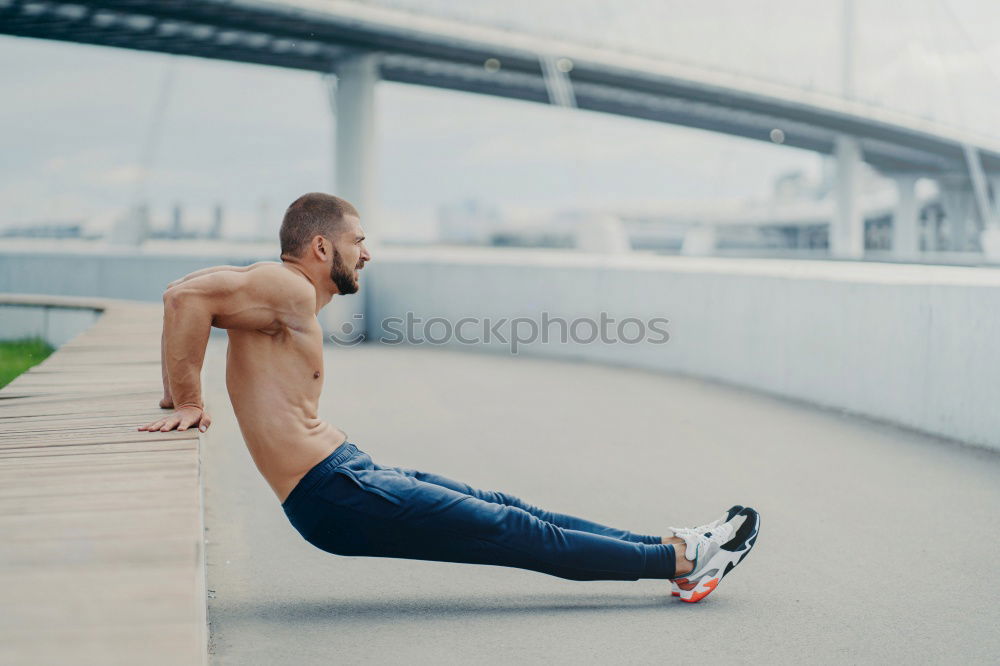 Seitenschuss eines muskulösen Mannes macht umgekehrte Push-up-Übung, trainiert die Arme, hält perfekten Körper und gute körperliche Form, trainiert aktiv im Freien, trägt Sporthosen und Turnschuhe, posiert auf der Brücke