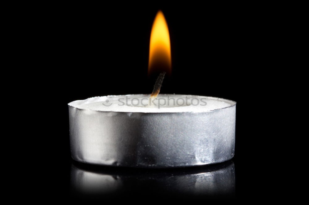 Black candle with a glowing flame isolated on a black background. Burning candle close-up