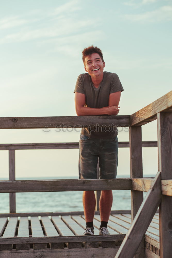 Smiling happy young man standing on a pier over the sea