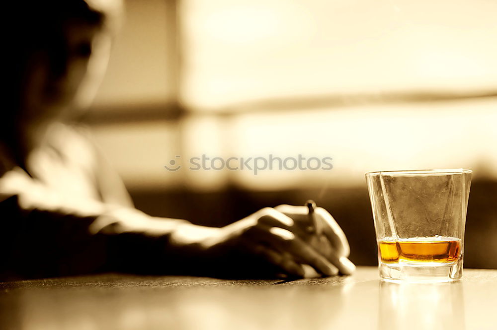 On a table there is a bottle of alcohol and a shot glass. A person’s hand is holding the shot glass.