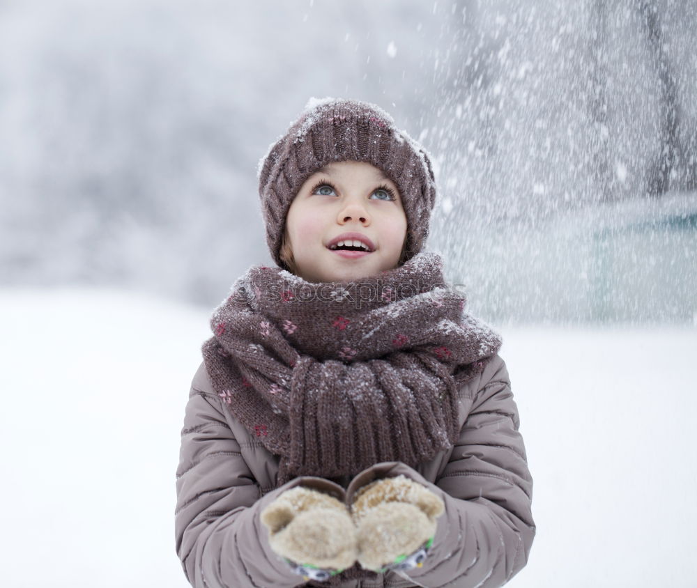 Little boy having fun playing with fresh snow during snowfall. Baby catching snowflakes on gloves. Kid dressed in warm clothes, hat, hand gloves and scarf. Active winter outdoors leisure for child