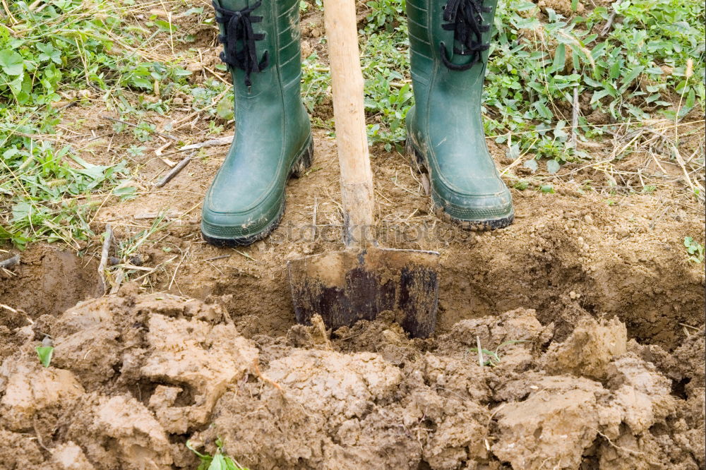 Legs in red trousers and green rubber boots jumping in a muddy puddle, so that the mud flies up