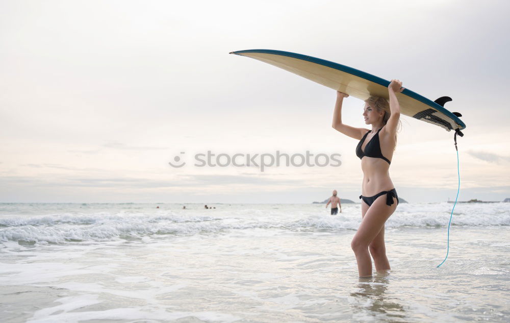 A young woman sitting under a surfboard