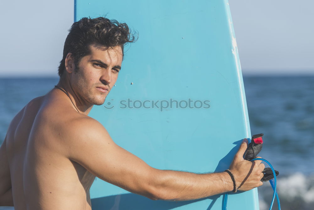 Young attractive surfer holding his surfboard at the beach