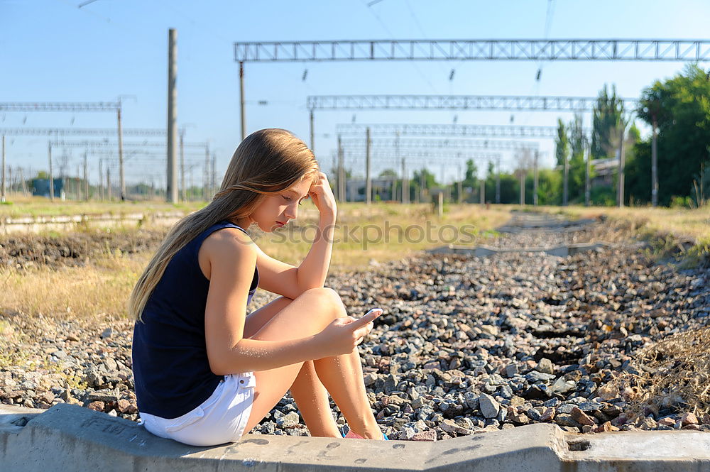 Sad girl teenager sitting on rusty rail track outside the town. Escape to be alone