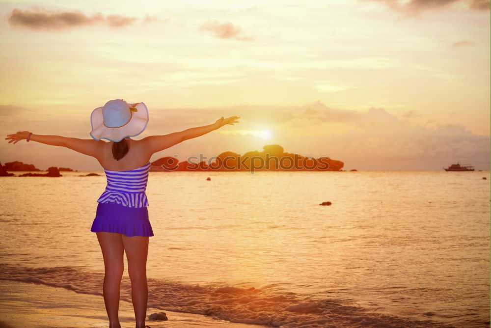 Smiling woman with sunglasses and hat raising arms happy with the sea in the background.