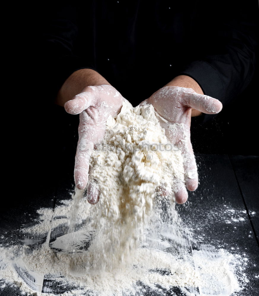 man sifts white wheat flour through a wooden sieve