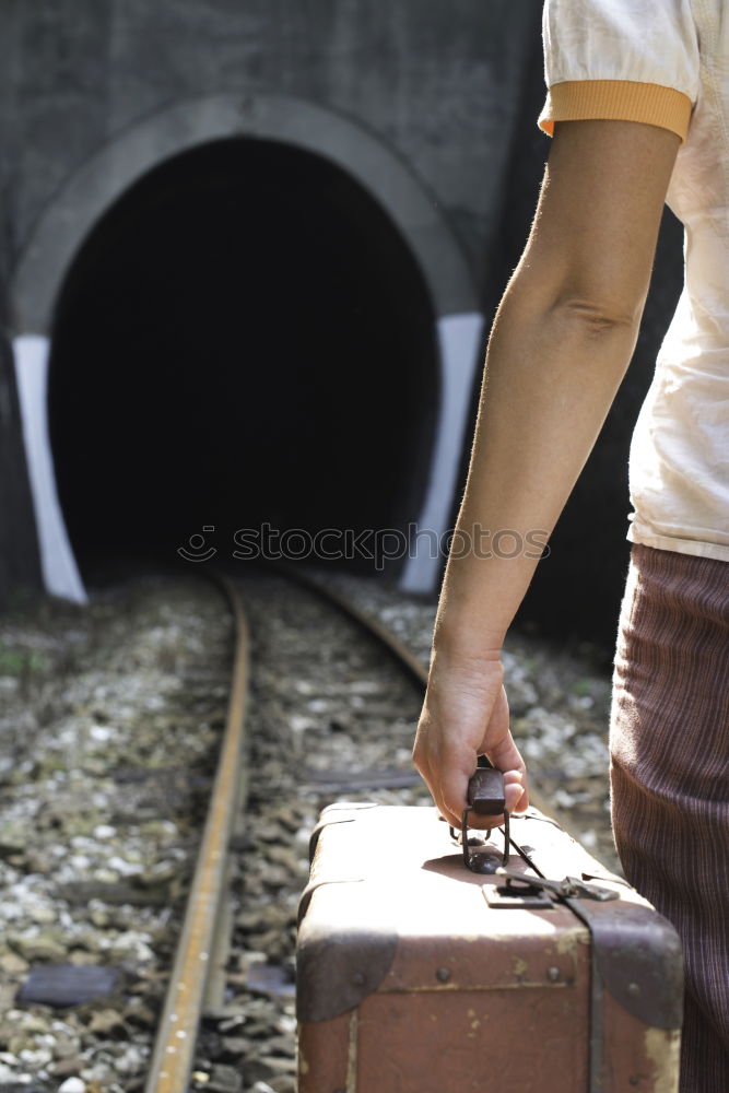 Woman and vintage suitcase on railway road and tunnel