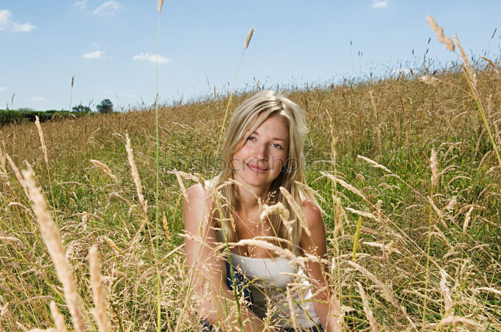 Similar – analogue portrait of a young woman sitting barefoot in a rye field in a summer dress and smiling