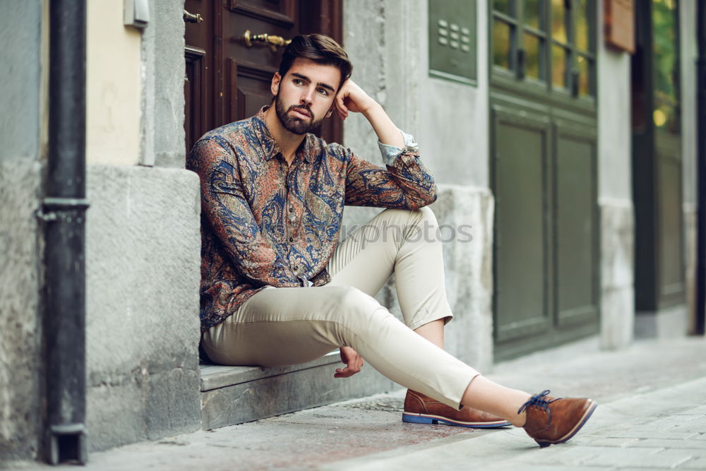 Young bearded man, model of fashion, sitting on urban step