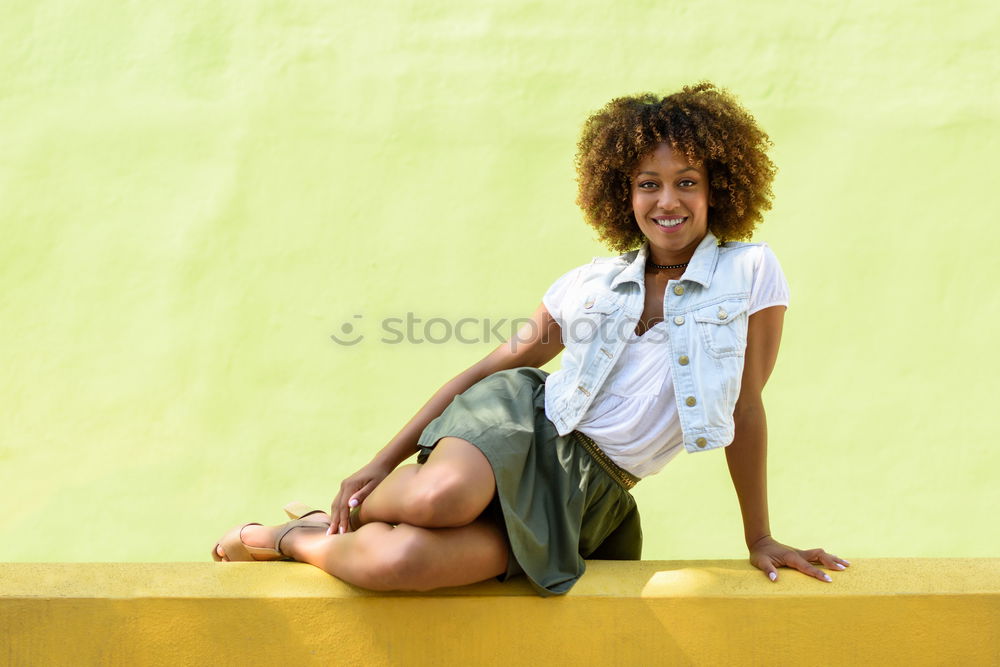 Young black woman, afro hairstyle, sitting on a wall smiling.