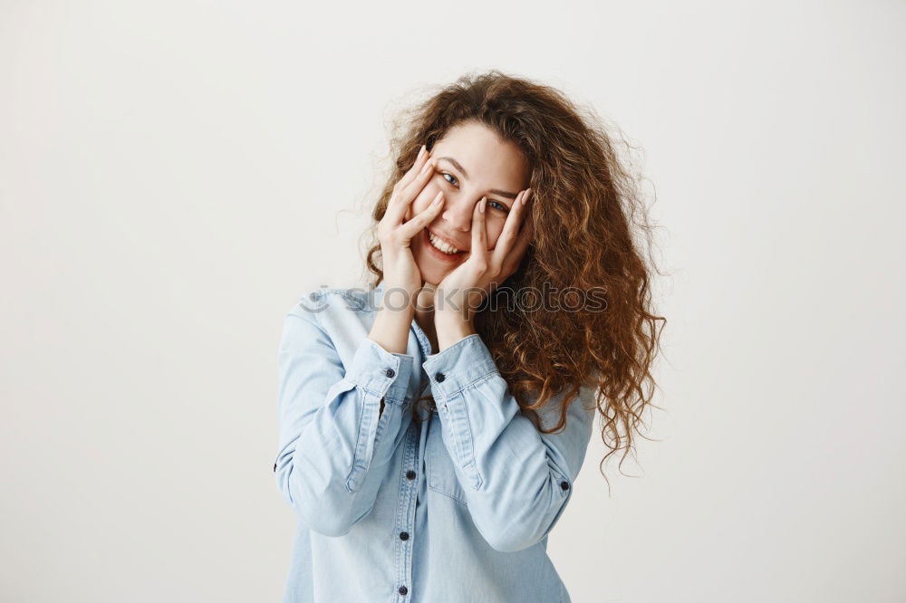 Woman with long red curly hair laughs looking at camera while holding a hand in front of her mouth