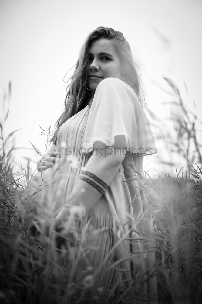 Similar – side portrait of young woman in summer dress sitting barefoot between bushes in nature