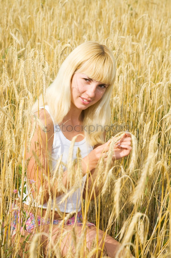 analogue portrait of a young woman sitting barefoot in a rye field in a summer dress and smiling