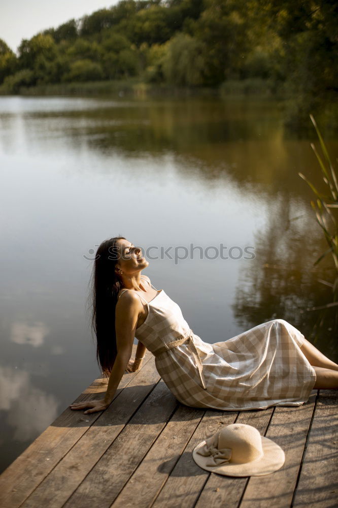 Similar – Young woman in a pink summer dress sitting in a clearing with her feet in the forest lake